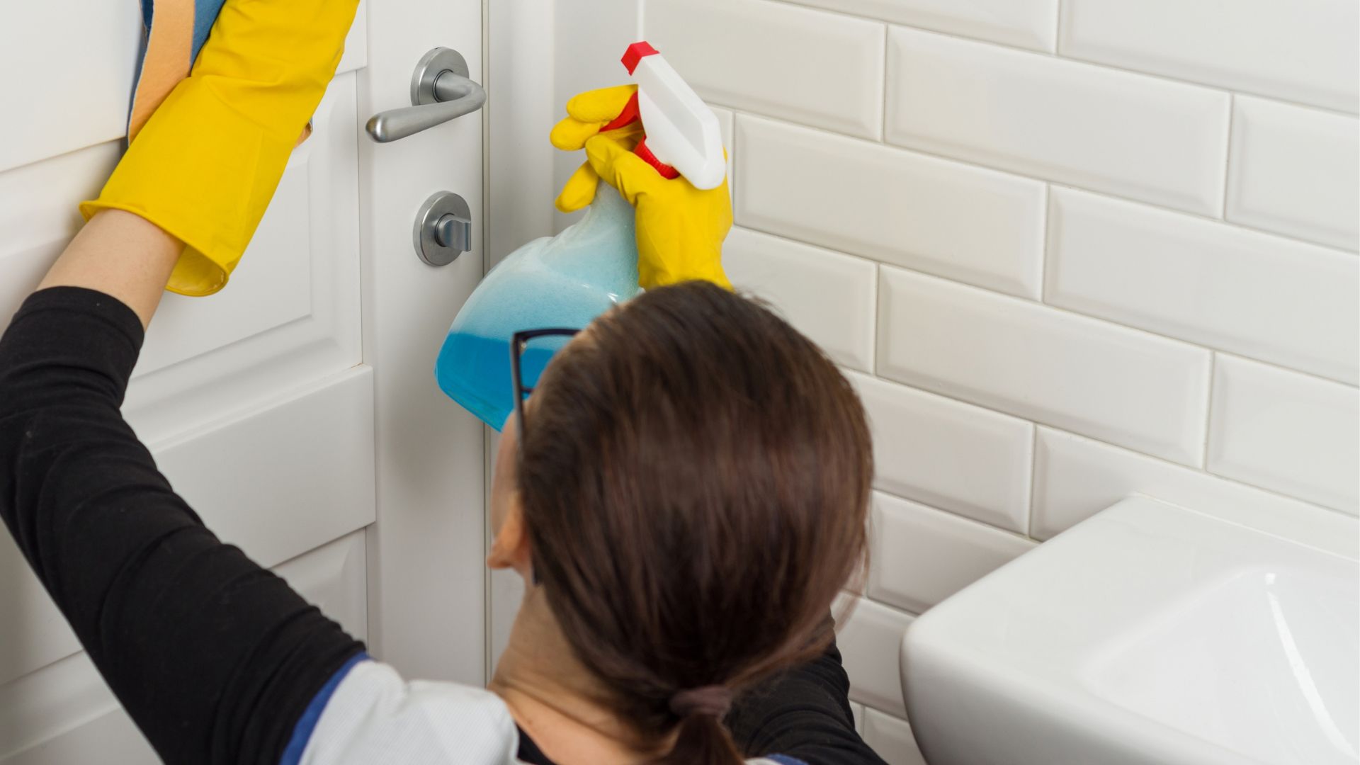 A woman cleaning a bathroom door with a spray bottle